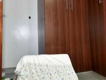 Video of a simple bedroom with a white bed, a white wall, and wooden wardrobe with a dark, textured finish, featuring a floral-patterned duvet.