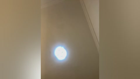 Video of a dimly lit, beige-painted corner with a bright, circular light source emitting a soft glow, casting a subtle shadow on the wall. The texture is smooth, and the lighting creates a serene, understated ambiance.
