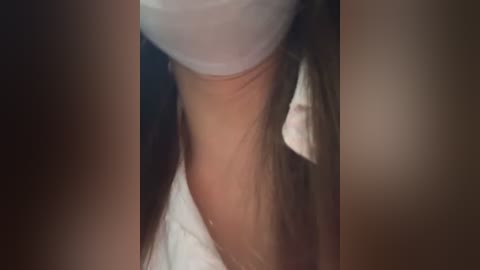Video of a close-up of a person's torso, showing smooth, light brown skin with a hint of a white shirt, long brown hair, and a blurred background.