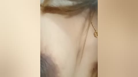 A close-up video of a woman's face with light skin and brown hair, wearing a delicate gold necklace with a pendant. The background is blurred, focusing on her features.