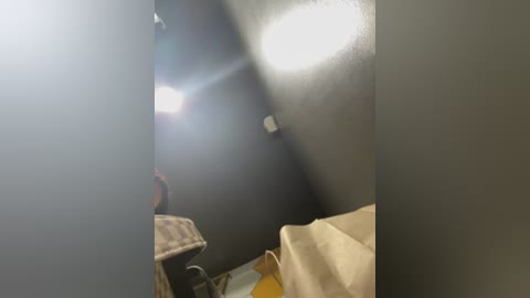 Video of a dimly lit, narrow hallway with gray walls, a small, bright light source above, and a partially visible person wearing a striped shirt and beige jacket.