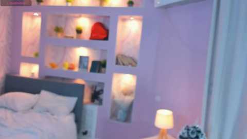 A video of a modern bedroom with lavender walls, a gray upholstered bed, and a white nightstand with a lamp. A built-in bookshelf with lights illuminates books, plants, and a red bag. The room has a cozy, elegant ambiance.