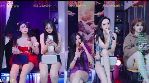 Video of five Asian women, diverse in age and style, seated on stools, singing into microphones, set against a colorful, modern background with banners and stage lights.