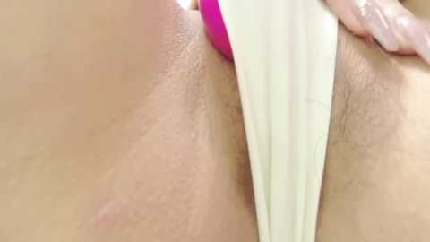Close-up video of a woman's bare pubic area, featuring a pink vibrator partially inserted into her vagina, wearing a white thong.