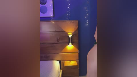 A video of a cozy bedroom with wooden furniture, warm yellow lighting, blue walls adorned with fairy lights, and a partially visible person's head.