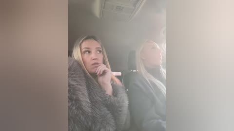 Media: Video of two blonde women in a car, one with a fur coat, the other with a jacket, looking out the window, blurry background.