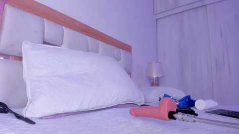 A video of a minimalist, white bedroom with a modern bed, white pillow, and a pink vibrator on the bed.