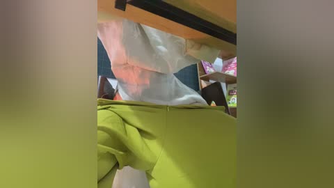 Video of a person wearing a white mask and a yellow shirt, with a blurred background of a room with shelves and boxes.