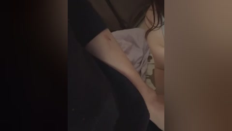 Video of a close-up of a woman with fair skin, wearing a light purple top and black pants, lying on a beige couch, with a dim, warm lighting creating a cozy atmosphere.