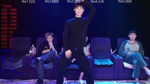 Video of a male dancer in black, performing on stage with three seated Asian men in casual attire, against a dimly lit backdrop.