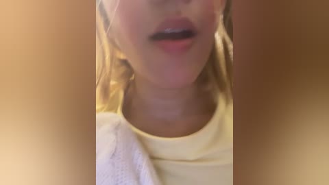 A close-up video of a woman's face with fair skin, light brown hair, wearing a yellow shirt. The background is blurred with a warm, golden hue.