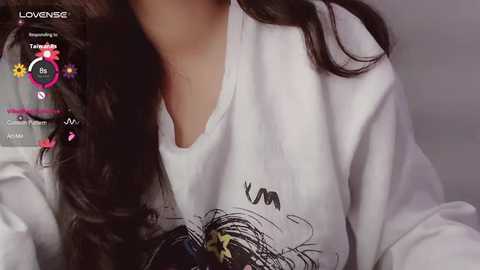 Video of a person's torso wearing a white long-sleeved shirt with a black graphic design, featuring a camel silhouette. The background is blurred, with a \"Lowen\" overlay displaying various icons and text.