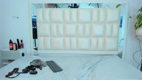 Video of a minimalist, modern bedroom with a white, padded headboard, a white bed, and a grey keyboard on the floor.