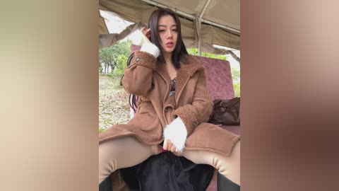 Media: Video of an Asian woman with shoulder-length black hair, wearing a brown fur coat, white gloves, and beige pants, sitting on a person's lap, outdoors.