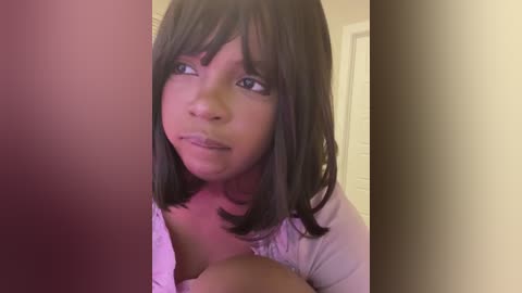 Video of a young African-American girl with medium brown skin, straight dark hair, and a serious expression. She wears a white top and stands in a beige hallway.