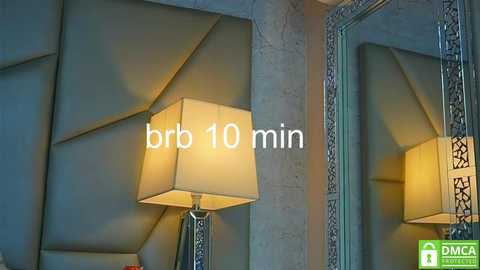 Video of a modern, stylish bedroom with a large, geometrically patterned wall, a mirror with a fancy frame, and a beige lampshade on a table. Text reads \"brb 10 min.\