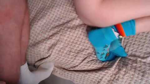 Video of a man's naked lower leg, wearing white socks, and a woman's lower body, wearing blue panties with a cartoon character design, lying on a beige, textured bedspread.