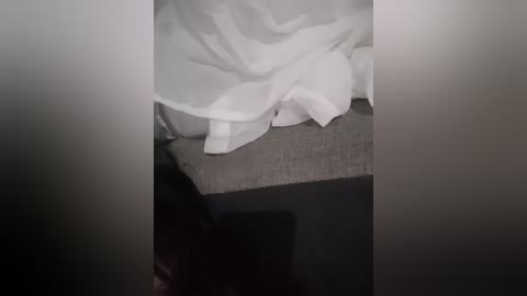 Media: A blurred video shows a white lace wedding gown draped over a grey fabric surface, with the bottom of the dress and part of the lace visible. The background is dark, making the white dress stand out.