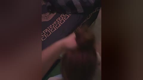 Video of a person wearing a dark blue shirt with white text and a circular emblem, leaning forward, blurred background.