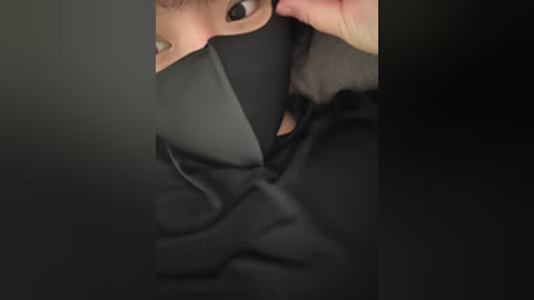 A close-up video of a person's face partially covered by a black cloth, revealing only the eyes and a small section of the nose. The background is blurred, focusing attention on the dark fabric.