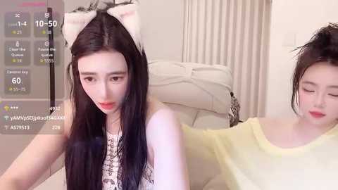 Video of a young East Asian woman with long black hair, wearing a white bow headband and a yellow top, lying on a bed.