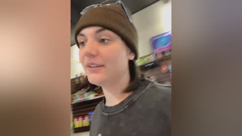A video of a young person with fair skin, wearing a brown knit hat, glasses, and a grey t-shirt, standing in a brightly lit convenience store.