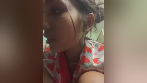 A close-up video of a young woman with medium skin tone and brown hair, wearing a pink shirt with red strawberry patterns. Her face is partially obscured by another person's arm, creating a blurred, intimate atmosphere.