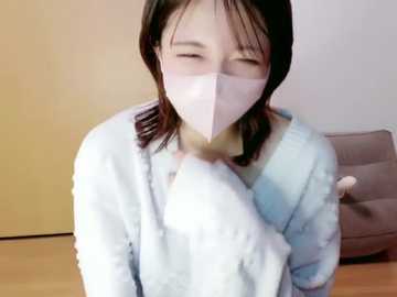Video of an Asian woman with straight black hair, wearing a light blue, fluffy robe and a white mask, sitting on a light-colored wooden floor, with a beige cushion in the background.