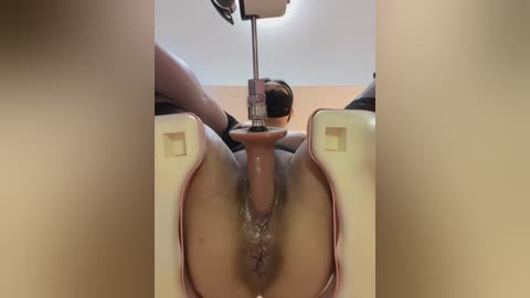 Video of a woman's shaved vulva, spread open, with a medical speculum inserted, in a clinical setting, under bright light.