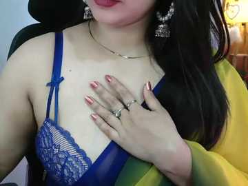 Video of a light-skinned woman with long black hair, wearing a blue lace bra and a yellow jacket, with a hand covering her chest.