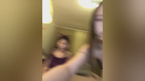 A blurry video shows a young woman in a pink nightgown, sitting on a bed with a pink wall behind her, partially obscured by a hand.