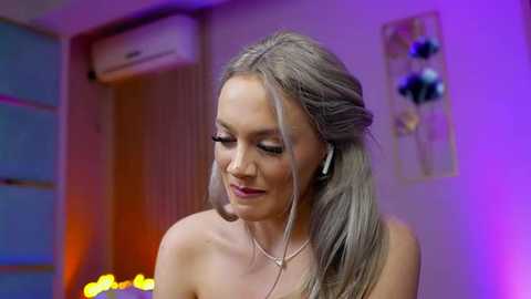 Video of a blonde woman with straight hair, wearing headphones, in a brightly lit room with purple and orange lighting.