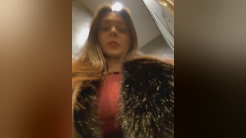 A video of a woman with long, straight, light brown hair, wearing a black fur jacket over a red top, captured from a low angle, slightly blurred.