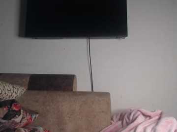 A video of a beige couch with a patterned cushion and a pink blanket, featuring a mounted flat-screen TV with a cord dangling from the ceiling.