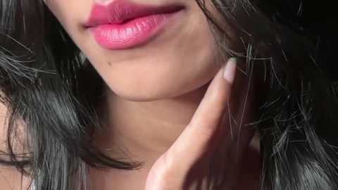 Close-up video of a woman with fair skin, glossy pink lips, and long dark hair. Her hand gently touches her neck, emphasizing her smooth skin texture.
