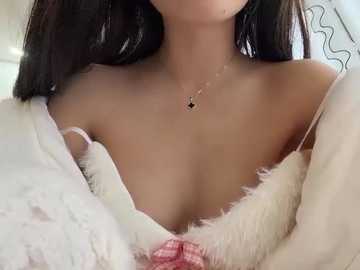 Video of a young Asian woman with medium-length black hair, wearing a white fur-lined robe that reveals her cleavage and a delicate necklace. Soft, natural lighting creates a cozy, intimate atmosphere.