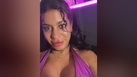 Video of a woman with light brown skin and curly black hair, wearing a purple halter top, looking sultry with a hint of pink lipstick.