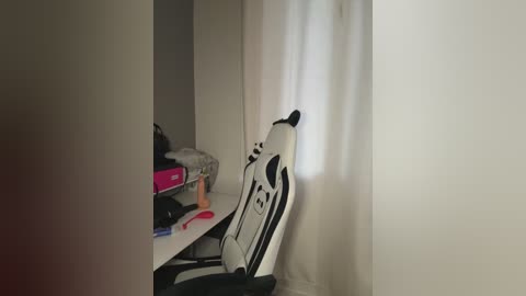 A video of a cluttered desk with a white gaming chair, a pink laptop case, and various office supplies, including scissors, pens, and a whiteboard marker, set against a plain white wall.