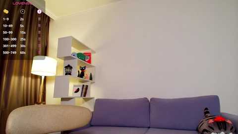 Video of a minimalist living room with a beige sofa, white shelving unit holding books and small figurines, and a brown lamp beside it.