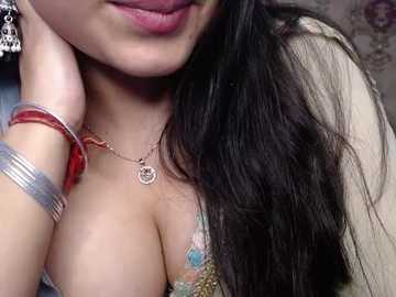 A close-up video of a South Asian woman with long black hair, wearing a colorful floral blouse and red bangles, showcasing her ample cleavage.