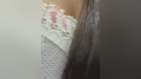 A close-up video of a woman's neck and chest, featuring a white lace bra with pink accents and her long, dark hair partially covering her left shoulder.