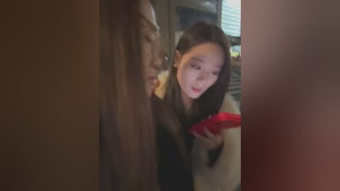 A blurred video of a young Asian woman with long black hair, wearing a beige coat, intently reading a red book, partially obscured by a large, dark figure.