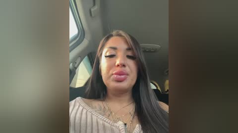 Video of a Latina woman with long dark hair, wearing a striped off-shoulder top, sticking her tongue out playfully inside a car.