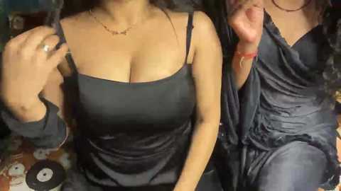 Video of two women, one in a black satin camisole, the other in a grey satin dress, with a man's erect penis between them.
