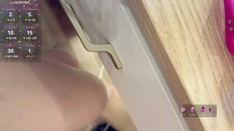 A close-up video shows a woman's chest with a large breast, partially covered by a white bra strap. The background is a wooden surface with a pink item visible.