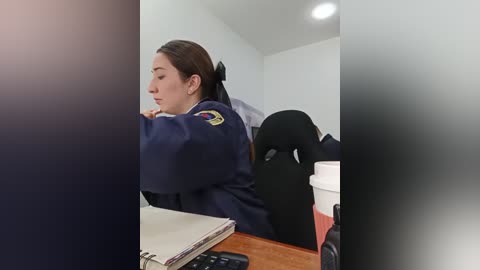 Media: Video of a Latina policewoman with dark hair in a ponytail, wearing a navy uniform with a badge, seated at a desk, sipping from a red coffee cup.