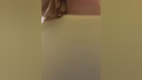 A close-up video of a person's face and shoulder, partially obscured by a yellow background. The subject has light skin and brown hair, with the hair visible near the top of the frame.