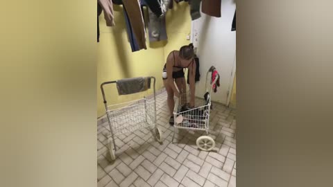 A video shows a woman with a prosthetic leg and a black bra, bending over a white shopping cart on a tiled floor, surrounded by hanging clothes in a yellow-painted room.