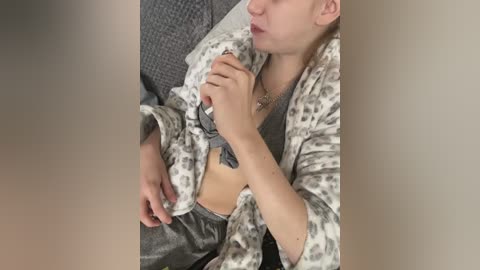 Video of a woman in a grey leopard print robe, revealing a tattoo on her right side. She has fair skin and short blonde hair.