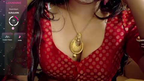 Video of a woman with medium skin tone, wearing a red, polka-dotted blouse with a plunging neckline revealing ample cleavage. She has long, dark hair and wears a gold pendant necklace.